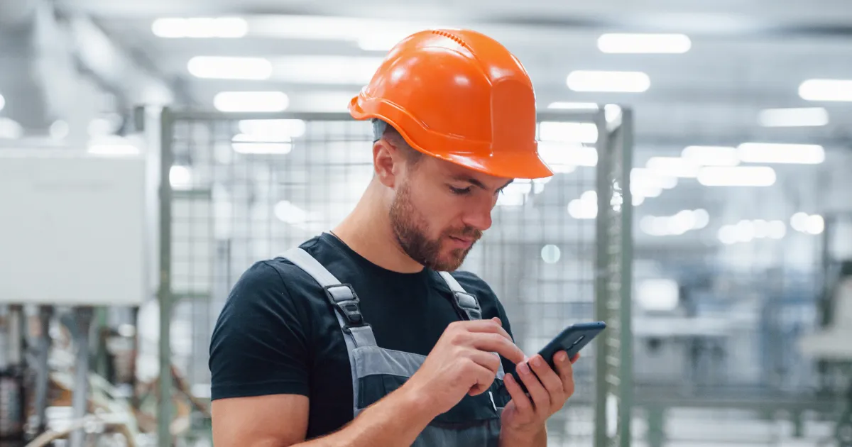 factory worker in an orange hard hat using a smartphone