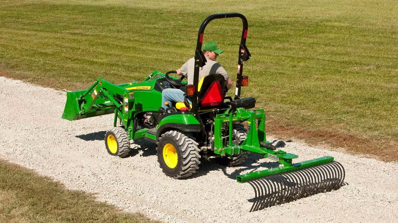 John Deere compact utility tractor with a landscape rake attached.