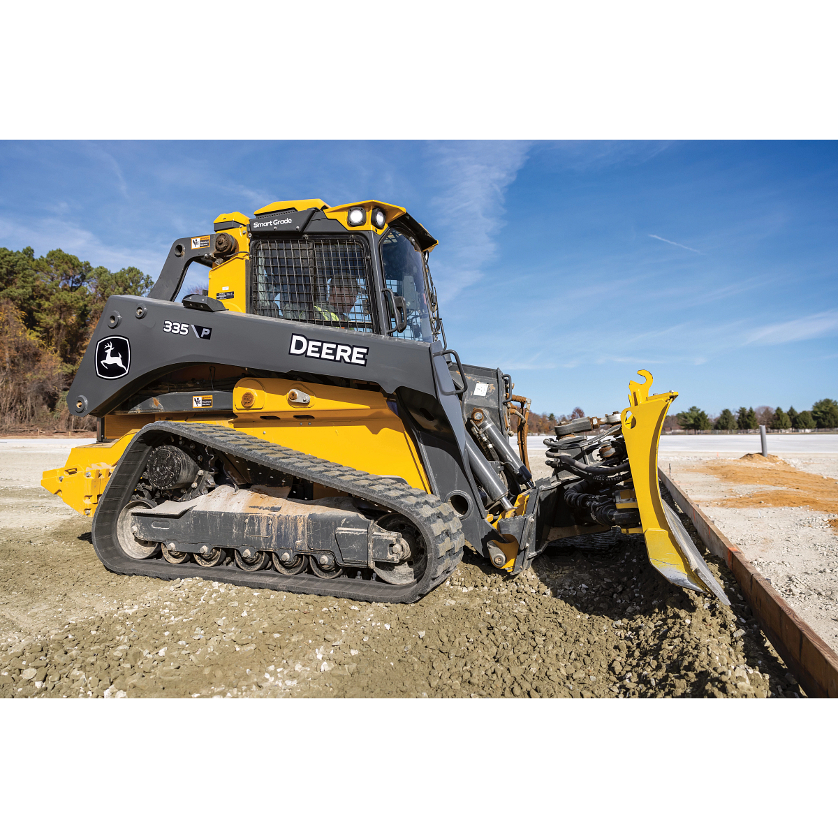 Side right view of a 335 P-Tier Compact Track Loader pushing gravel and forms into place on a jobsite