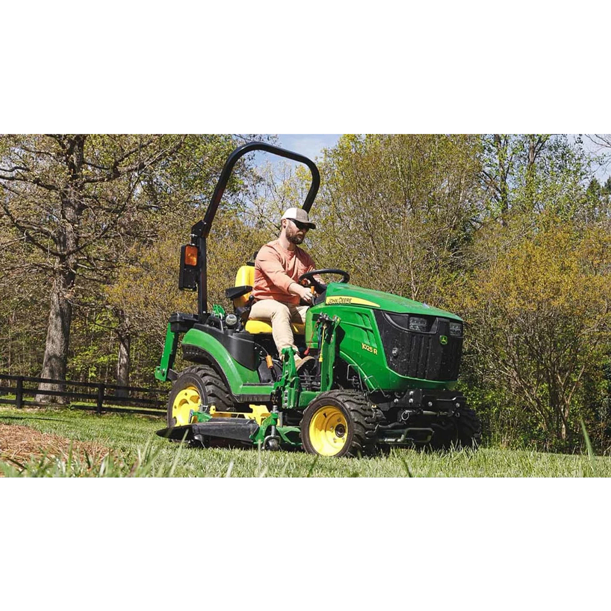 1025R Tractor Sub-Compact Tractors with a farmer riding on a green tractor in a field