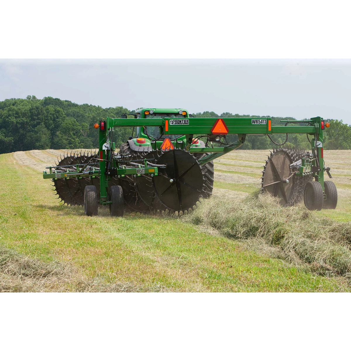 Rear view of a WR5417 wheel rake and tractor raking windrows in a tree-lined hay field