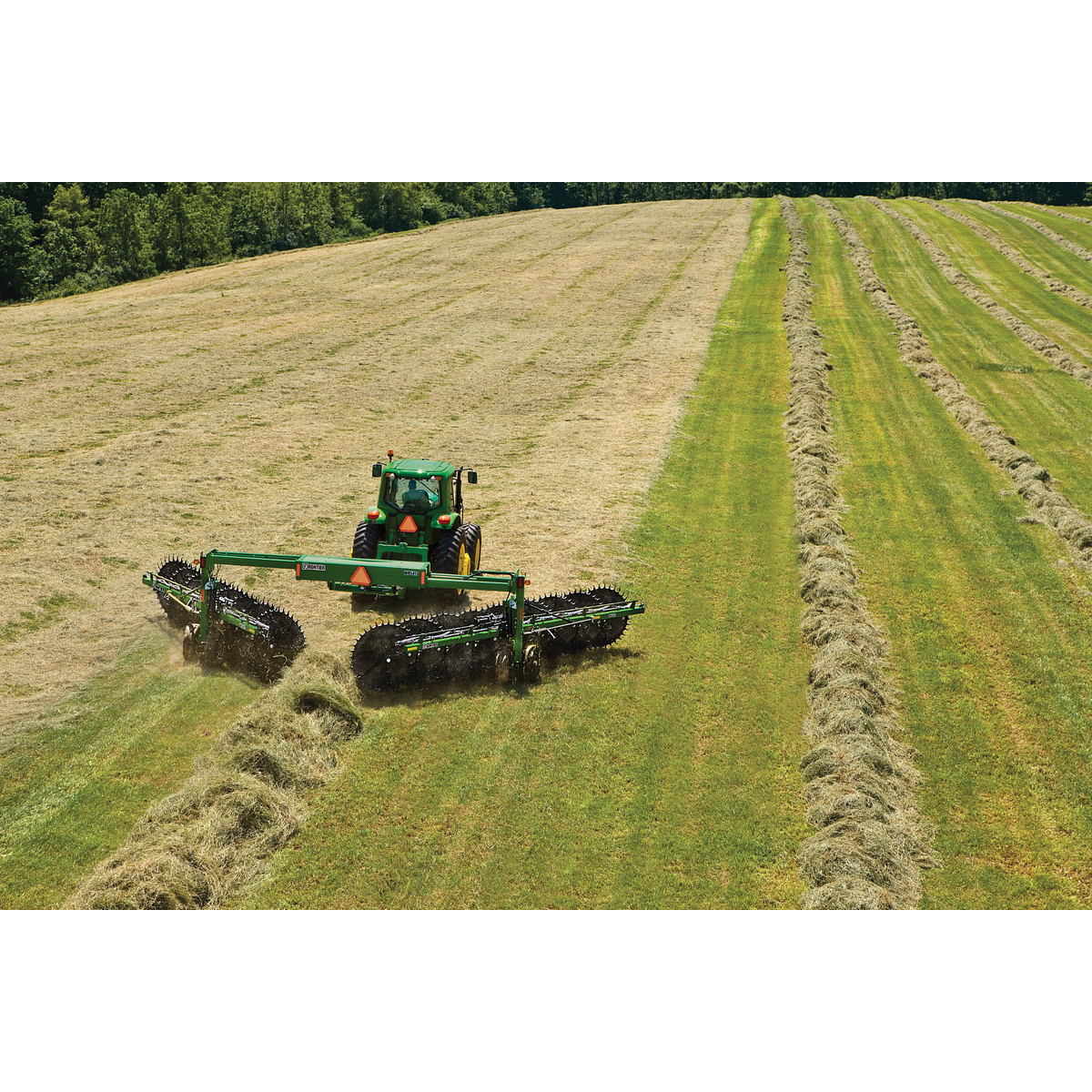 Rear aerial view of a tractor using a WR5417 wheel rake to form windrows of hay in a green field
