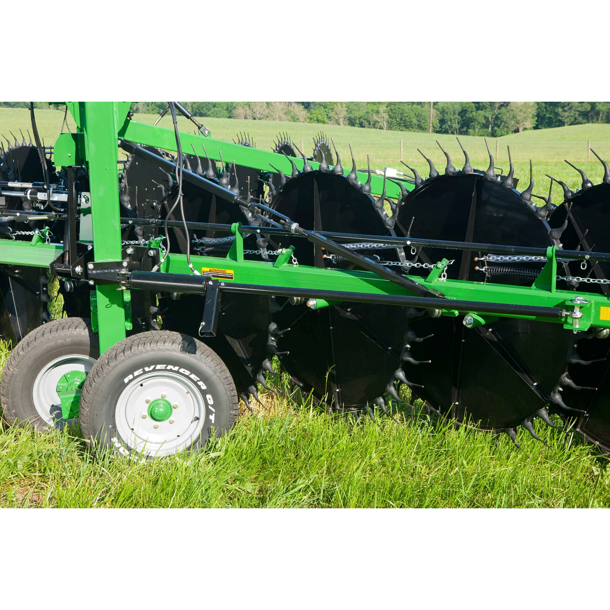 Side close-up of a WR High-Capacity Wheel Rake's black circular components, frame, and wheels parked in grass