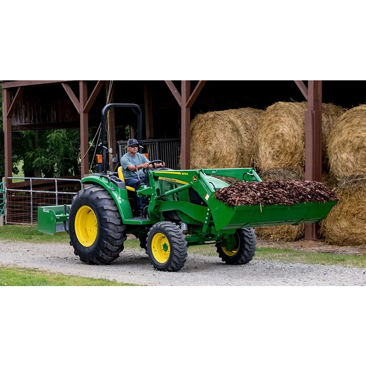 farmer operating a 4044M Compact Tractor to move mulch in front of hay bales