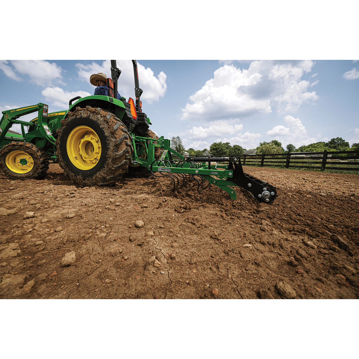 Side left view of a 4044M tractor with 400E loader dragging a PF5072 Pro Finisher across a fenced-in, dirt paddock