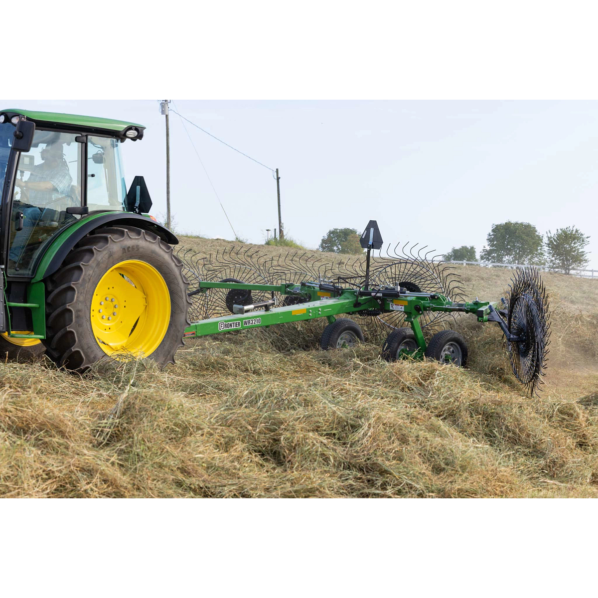 Side left closeup of a 5125M tractor pulling a WR3210 wheel rake through thick felled hay
