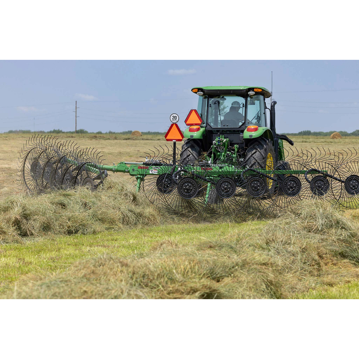 Rear view of a 5100E tractor working a hay field with a WR3212 wheel rake