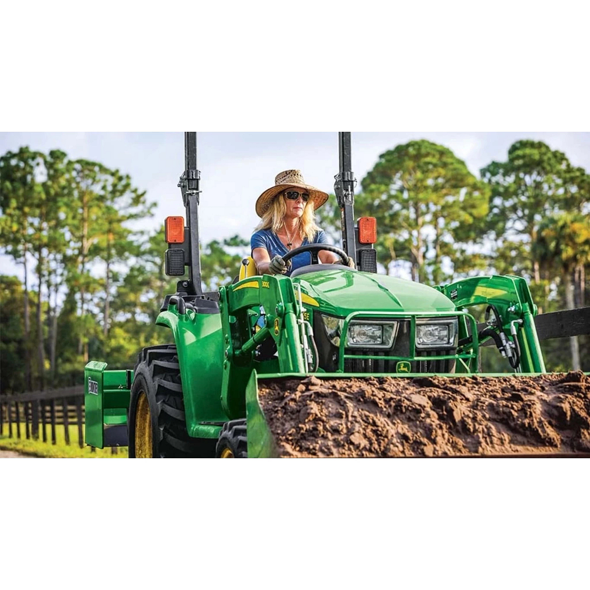3025E 3 Series Compact Tractors with an operator driving a tractor in a field with a large pile of dirt