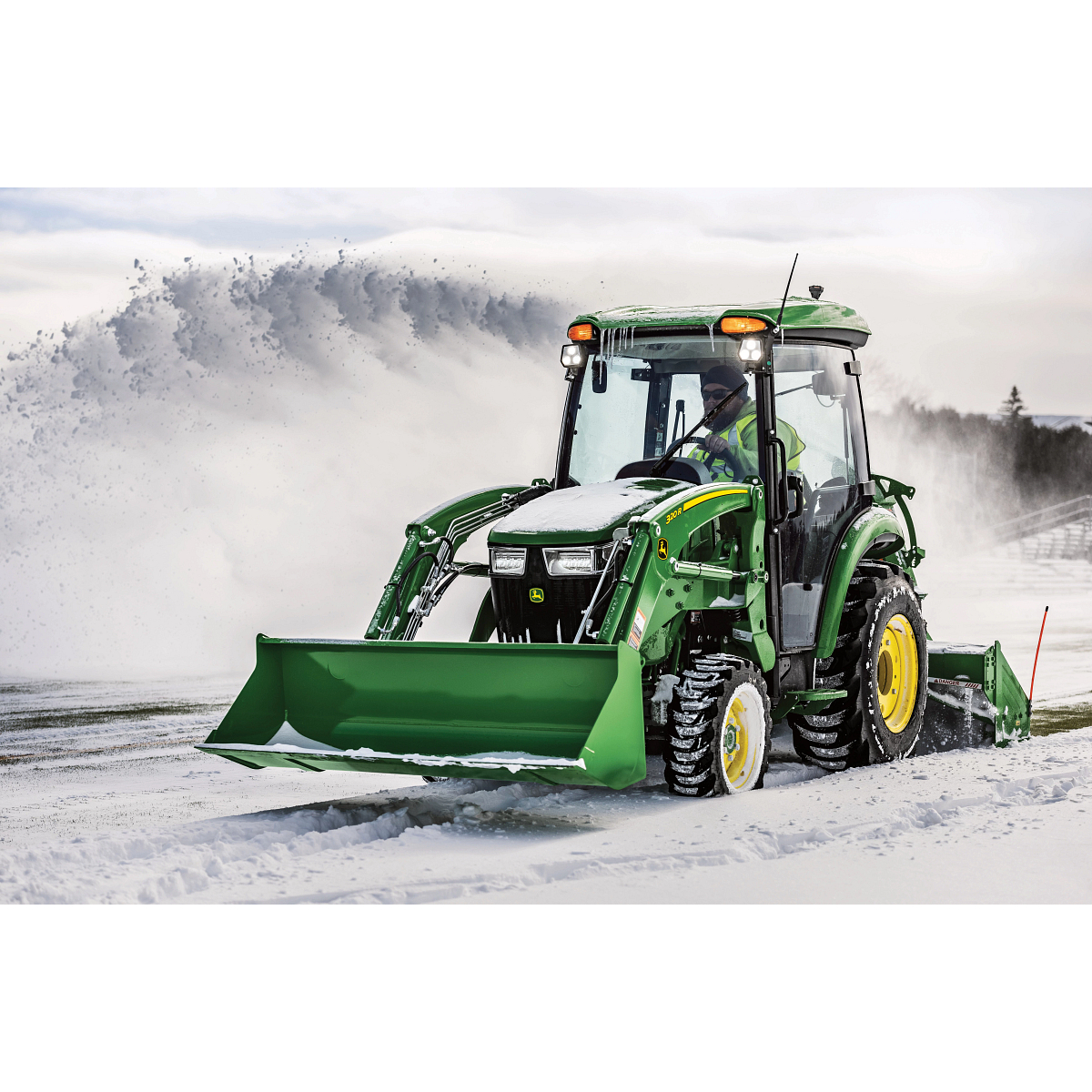 Front left view of a green 3046R compact utility tractor with 320R loader attachment snow blowing a road with rear-attached SB1164P snowblower