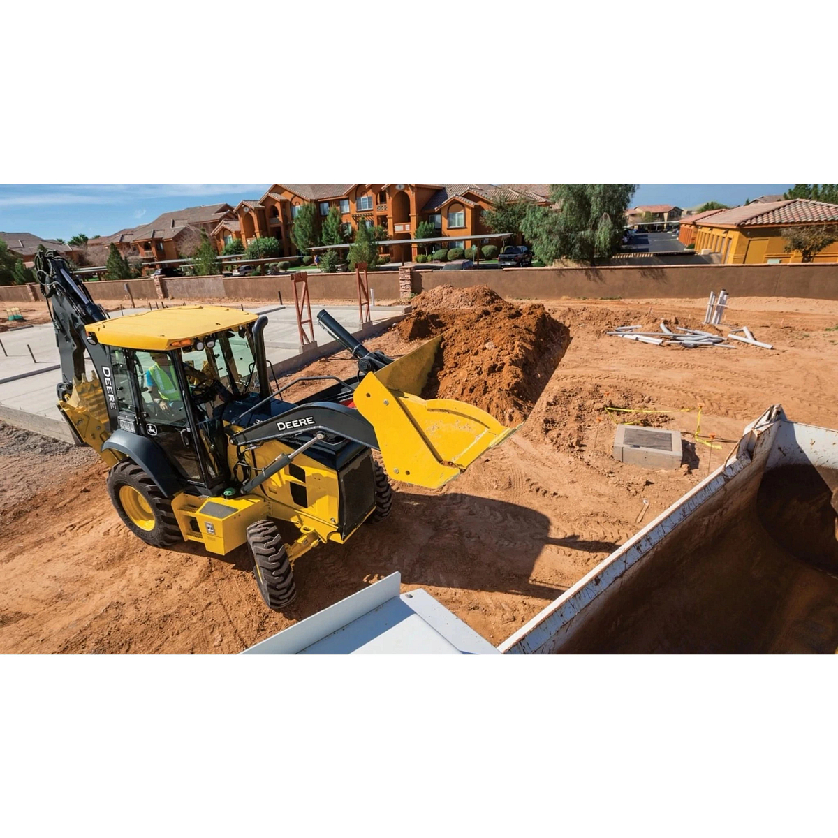310 G-Tier Backhoe Loader loading dirt into a dump truck in a construction site