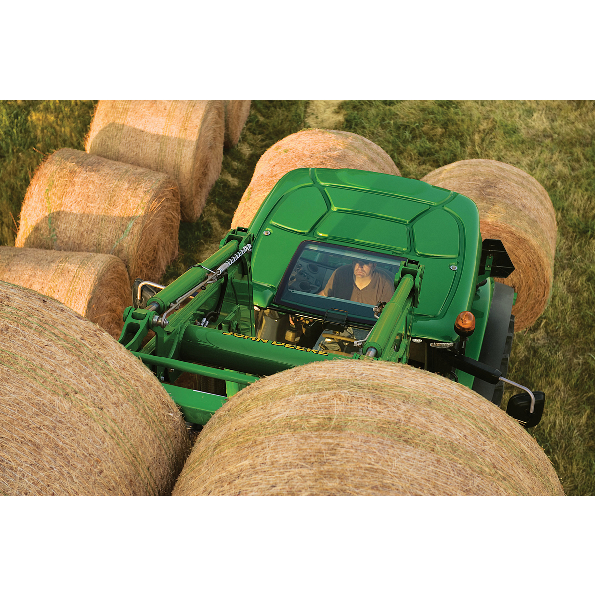 A tractor with a bale spear attachment surrounded by large, round hay bales in a field