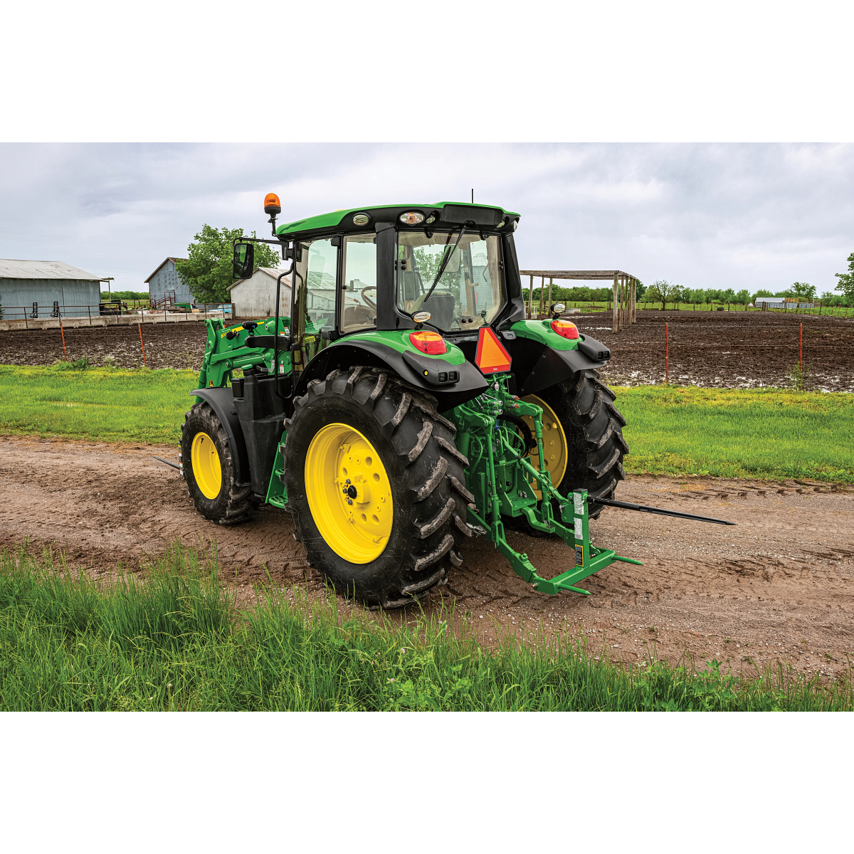 A tractor with a bale spear on a dirt road near crop fields