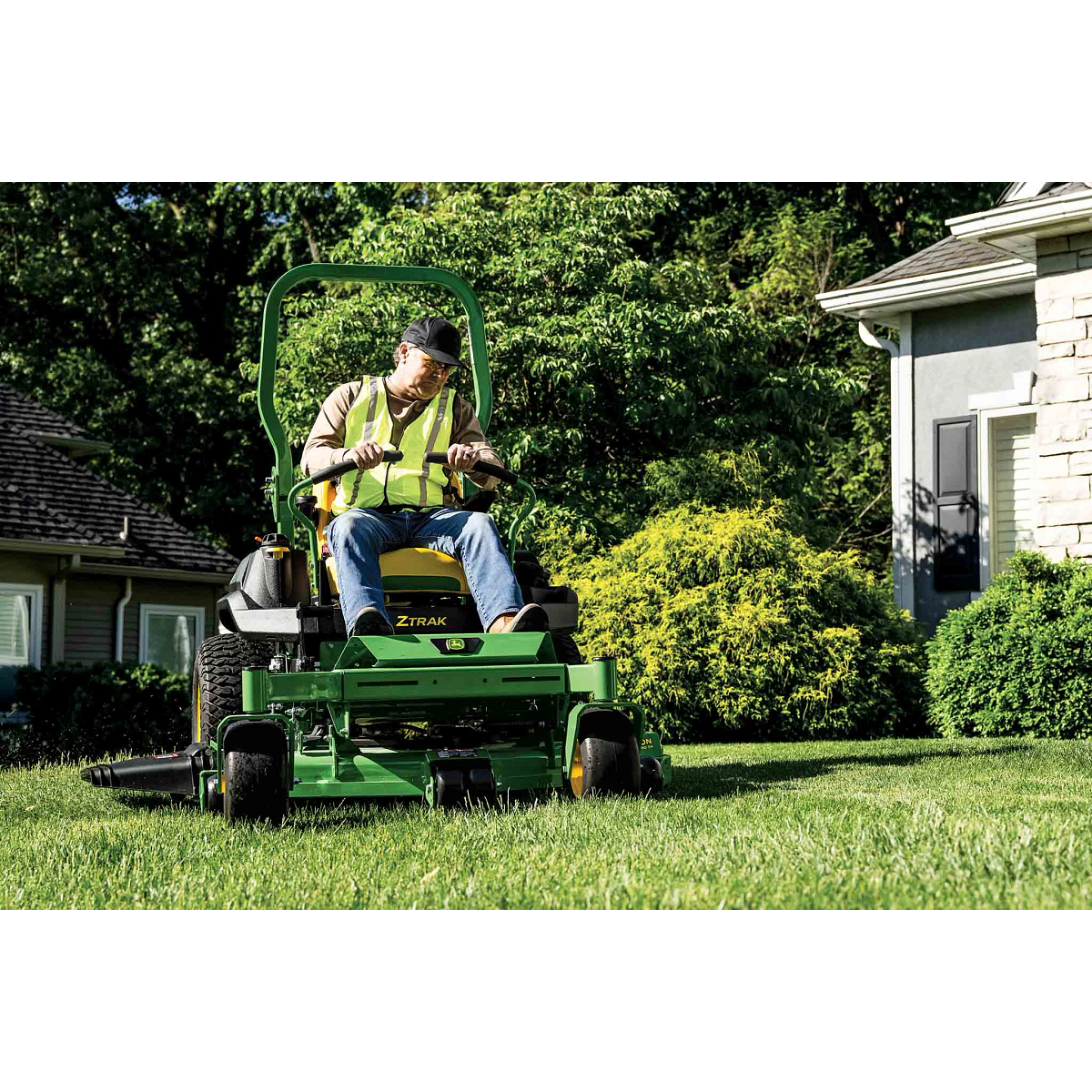 Grass being mowed in front of a residence by a landscaper on a green zero-turn mower.