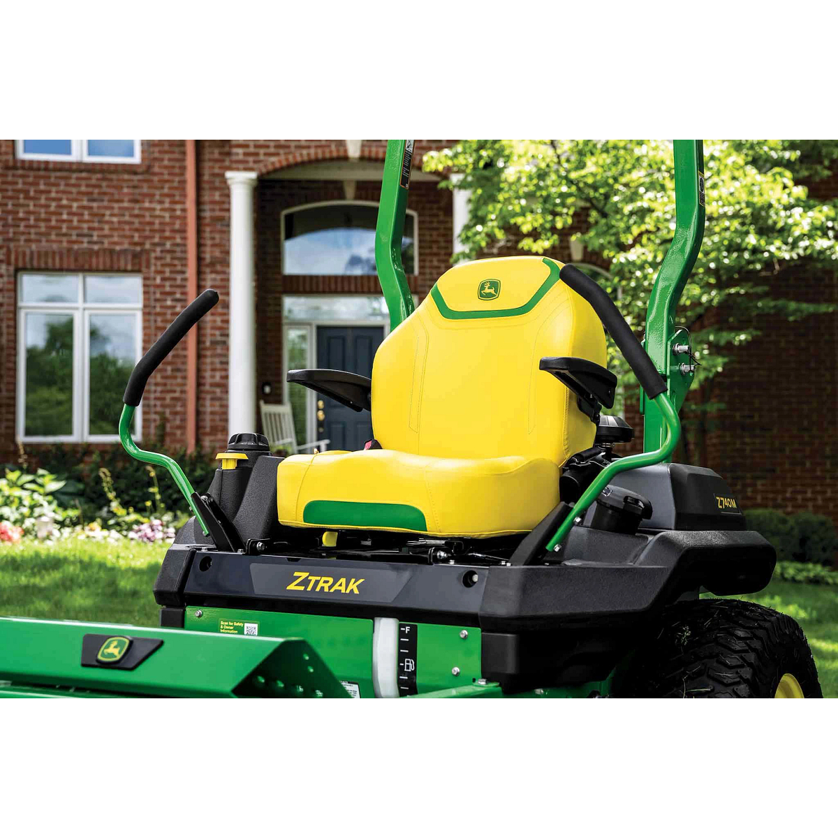 A zoomed-in shot of a yellow zero-turn mower seat with green detailing in front of a residence.