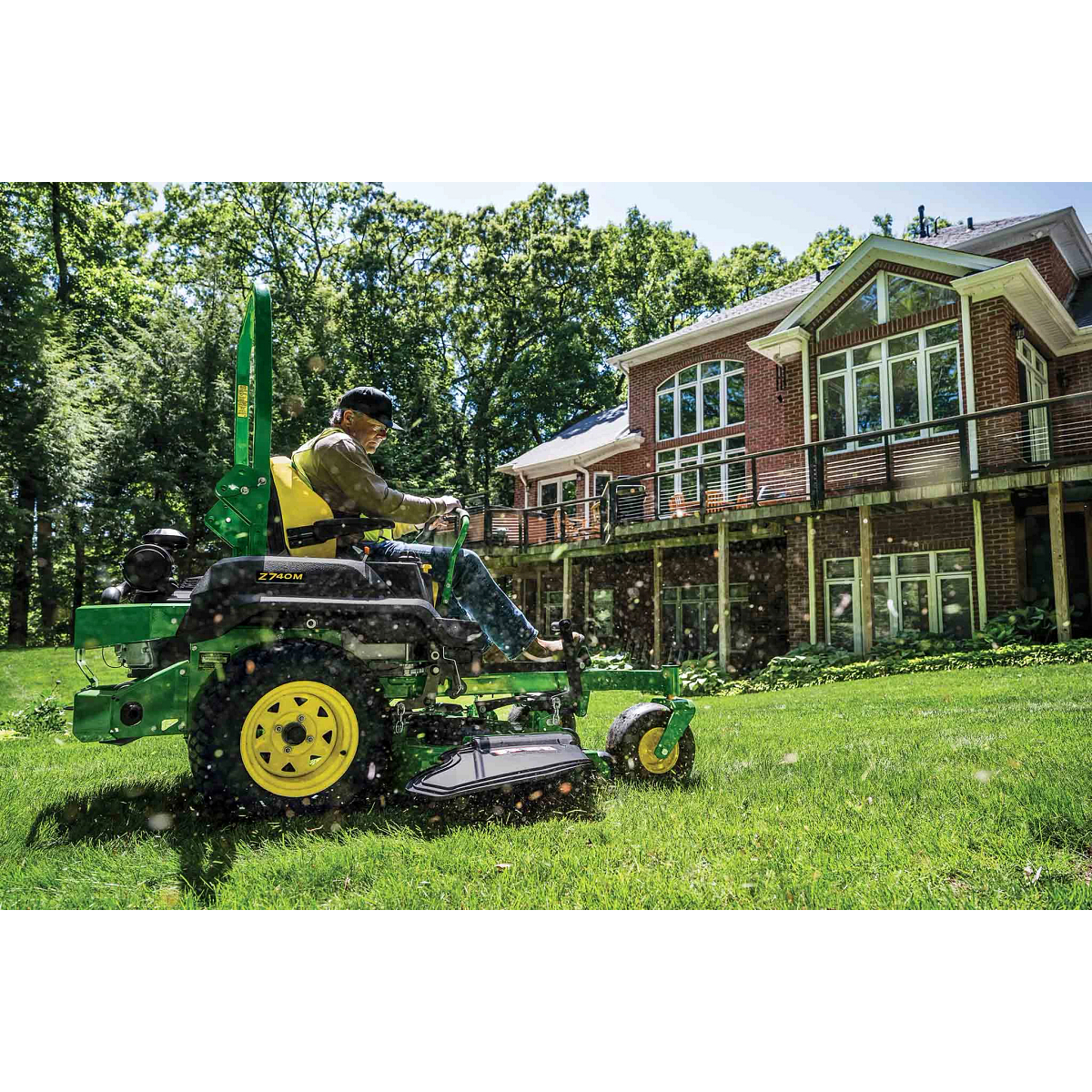 Person operating a Z740M zero-turn mower on a lush lawn beside a brick home surrounded by mature trees on a sunny day