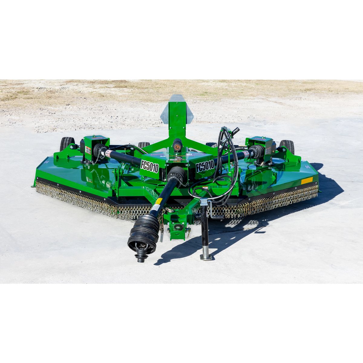 Front view of a green Frontier FC5010 dual-spindle rotary cutter with a PTO driveline, hydraulic hoses, safety chain shielding, and transport wheels, positioned on a concrete surface outdoors