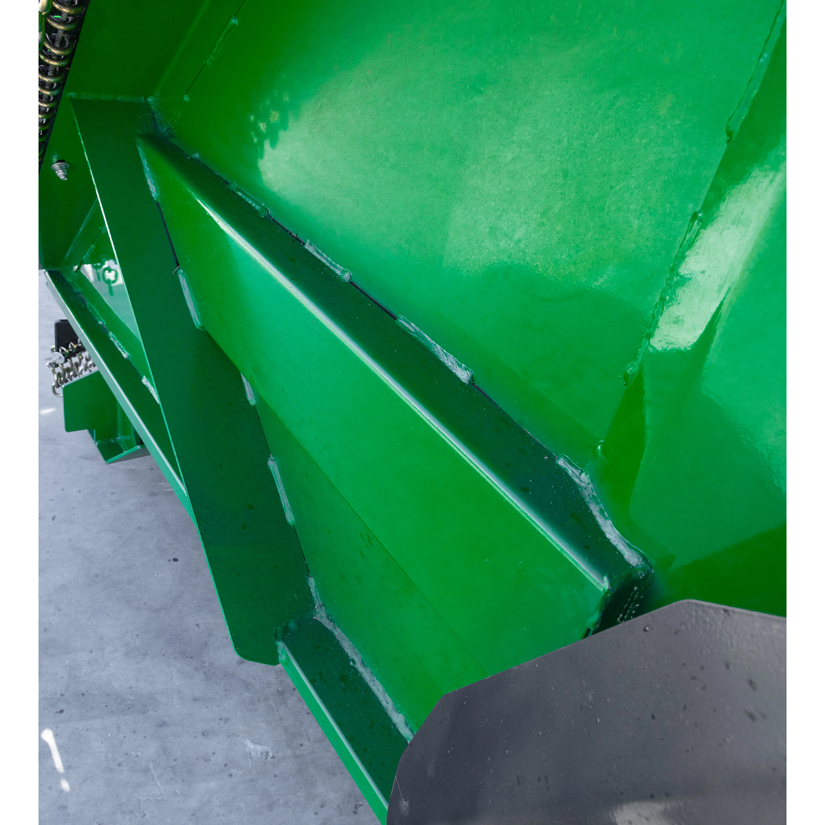 Close-up of a green steel mower deck showing reinforced welded panels and smooth painted surfaces on a rotary cutter attachment
