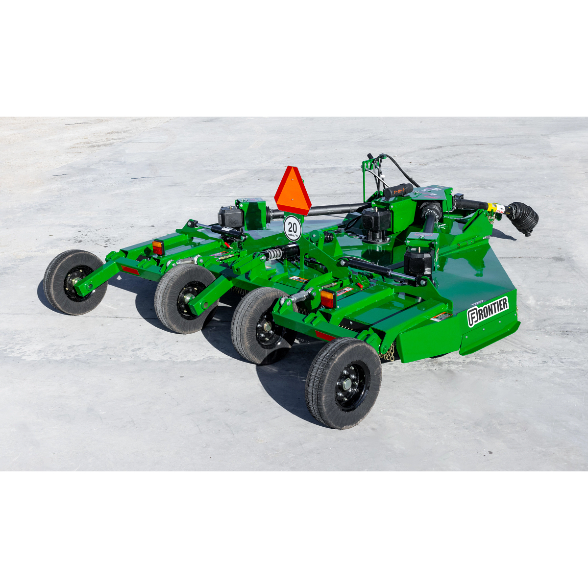 Rear three-quarter view of a green Frontier rotary cutter with four transport wheels, PTO driveline, hydraulic components, safety chain shielding, and a slow-moving vehicle emblem, parked on a concrete surface outdoors