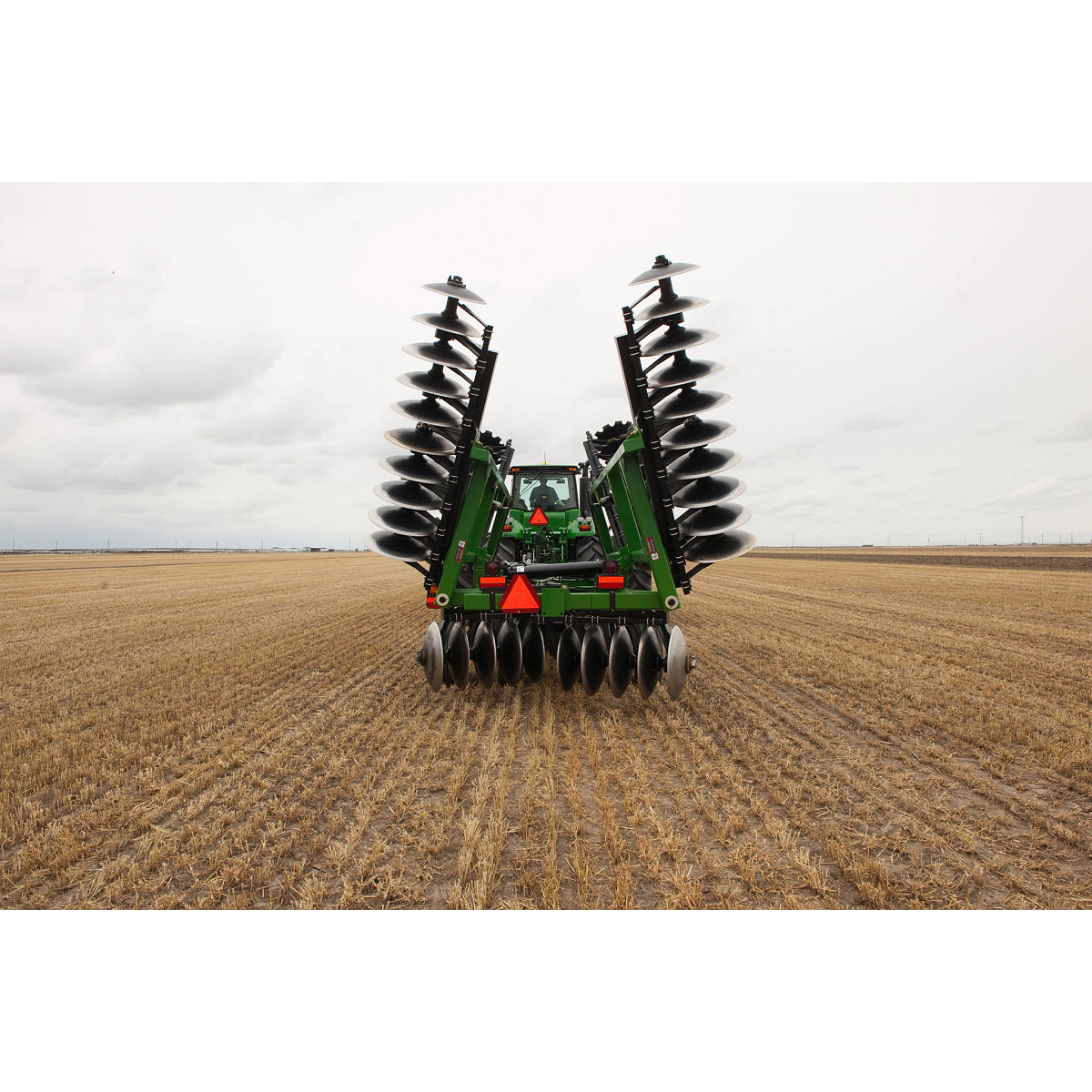 Distant rear view of a tractor pulling a Frontier Tandem 51 Series Disk Harrow in the field