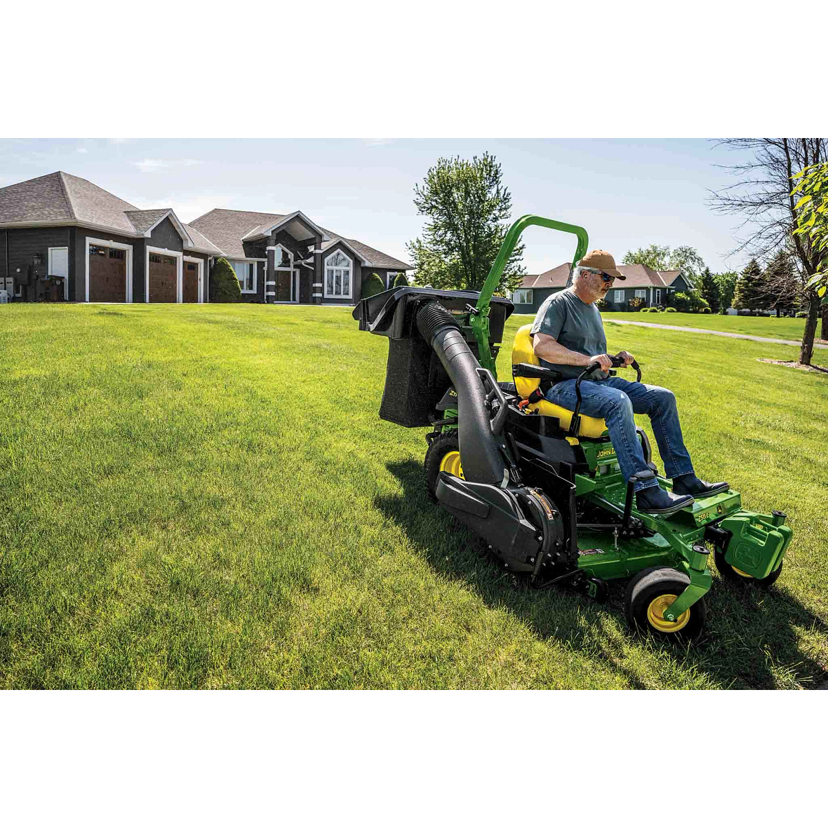 A Z515E zero-turn mower with a bagging attachment mows a wide-open lawn in front of a residence.