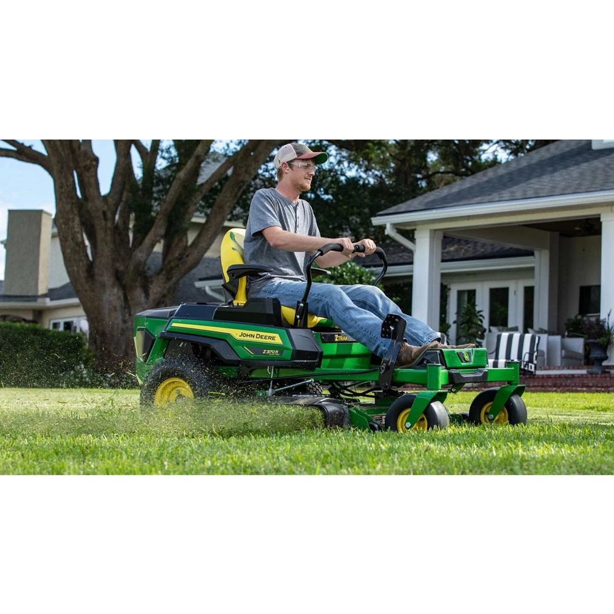 A farmer riding on a green lawn mower in front of a house