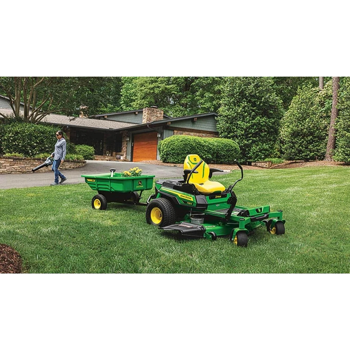 Homeowner using a leaf blower on a driveway with a Z380R Electric ZTrak Mower and wagon in the foreground
