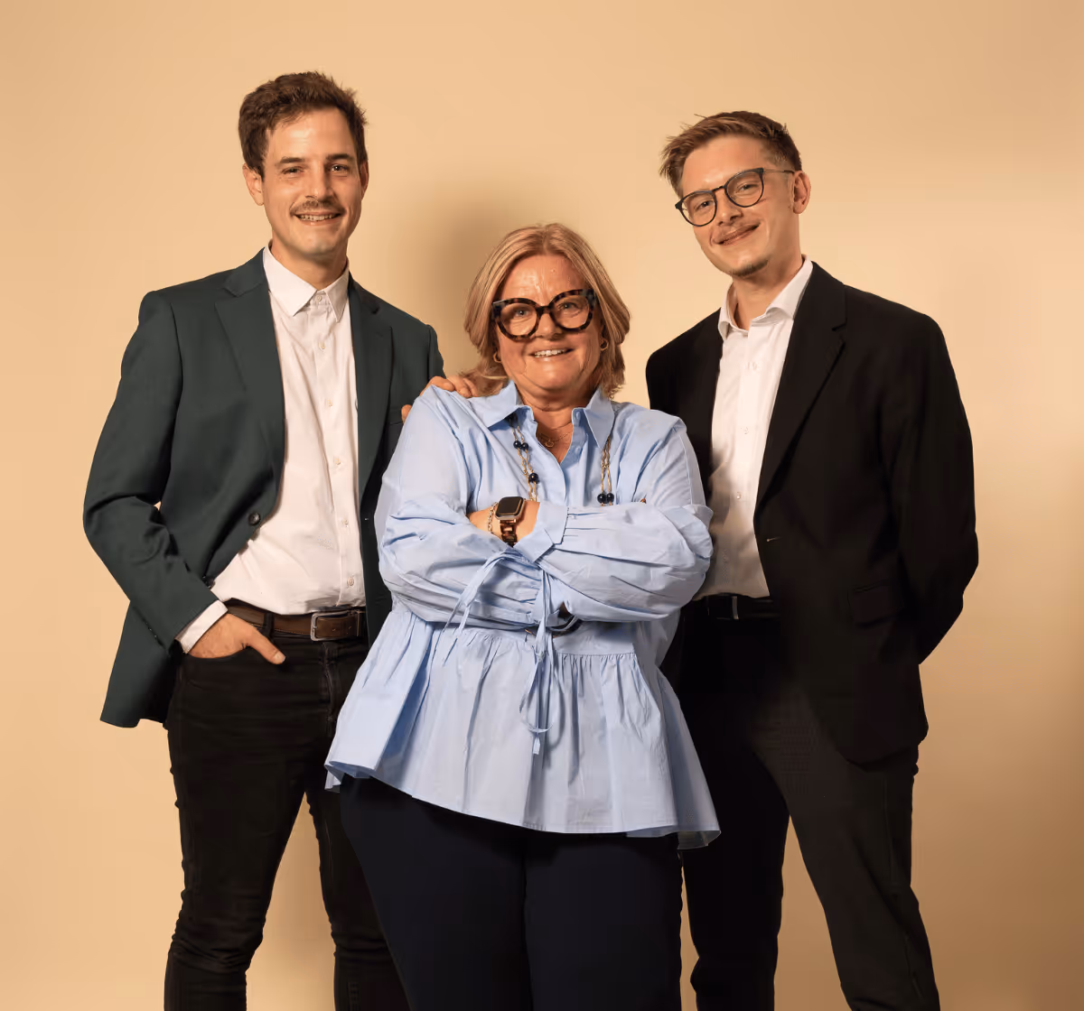 Groupe de deux hommes en costume et une femme avec chemisier bleu et lunettes, posant ensemble devant un fond beige.