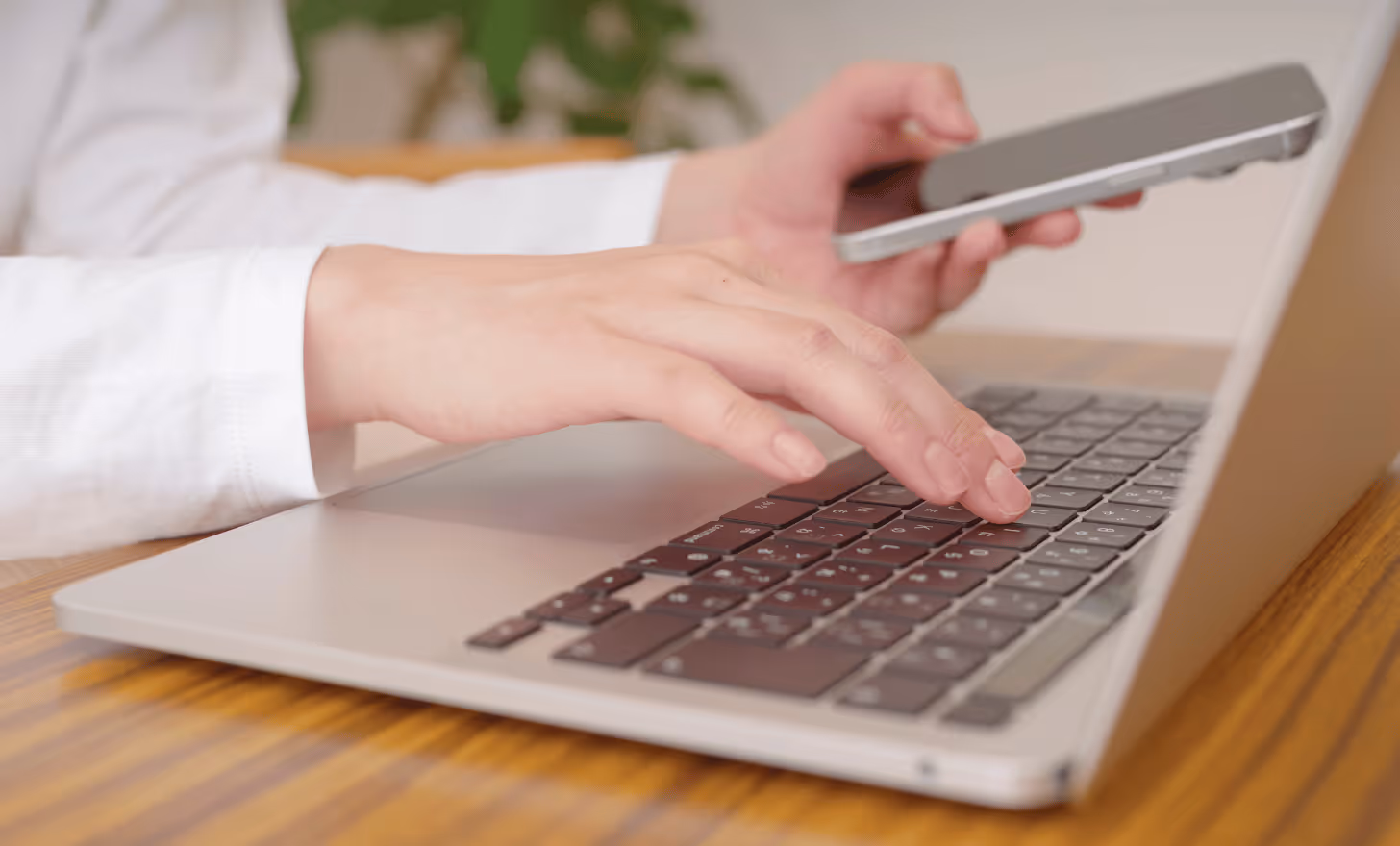 Une personne tapant sur un clavier d'ordinateur portable tout en tenant un smartphone dans l'autre main.