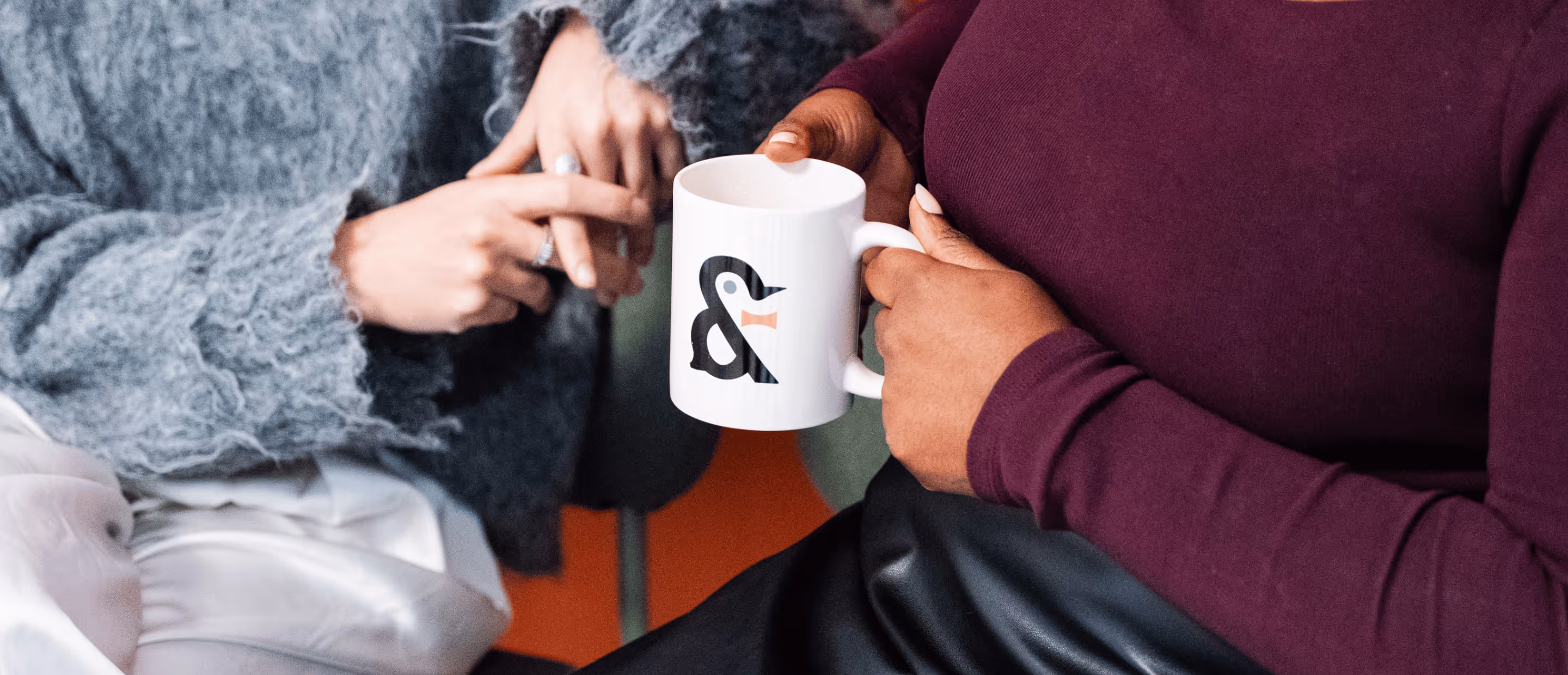Deux personnes discutant, l'une tenant une tasse blanche avec un symbole & stylisé noir et orange.