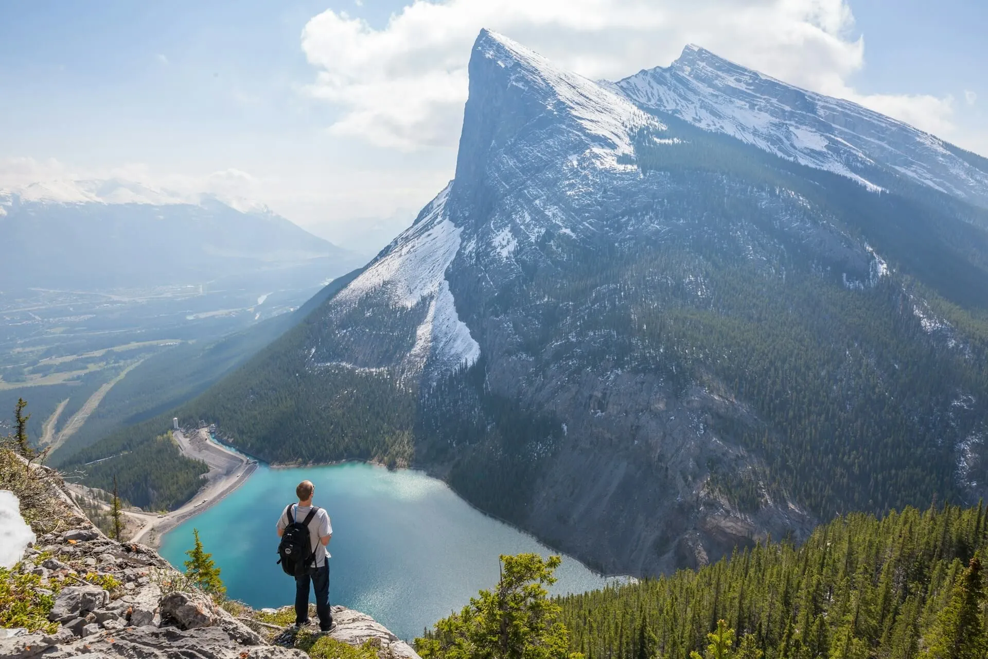 man standing at the top of a glacial lake looking down with mountain in the background