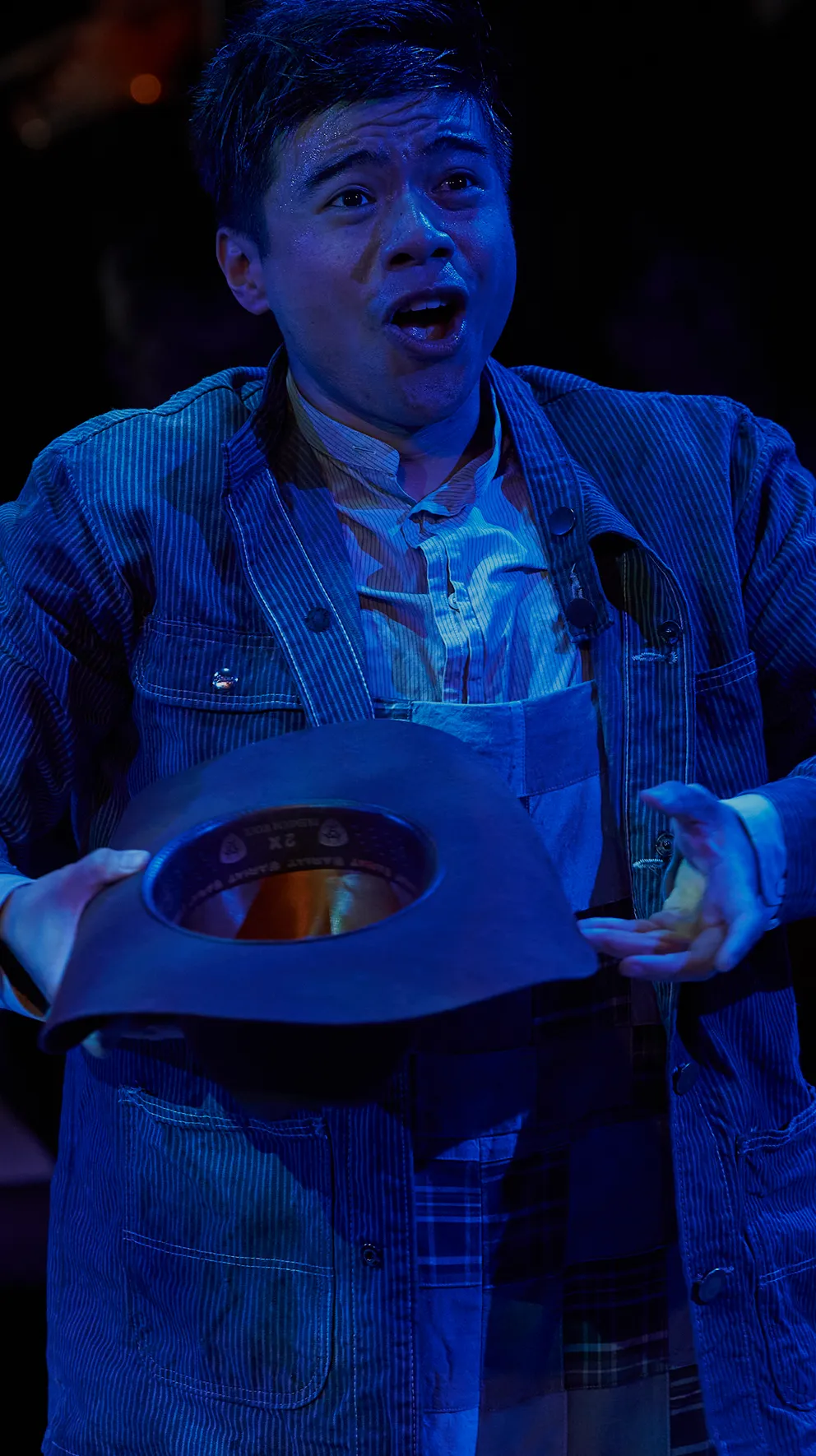 Male performer under blue lighting holding a hat mid-performance.