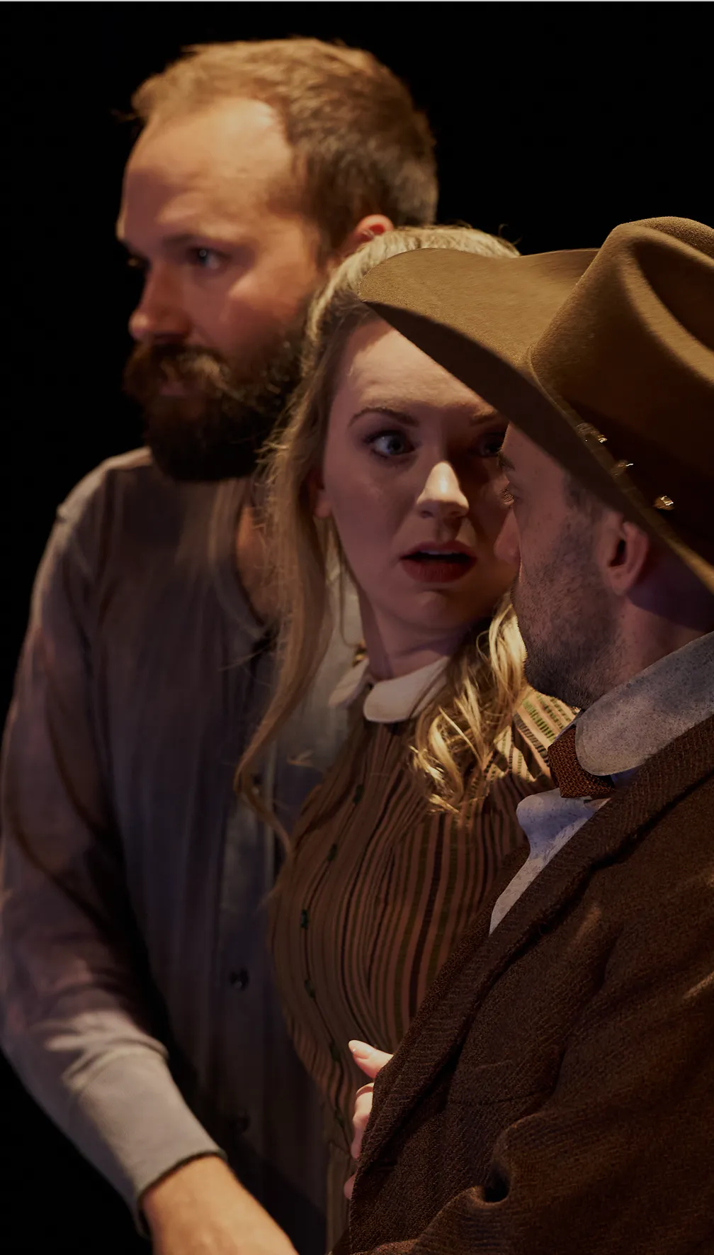 Three actors in period costumes reacting emotionally on stage.