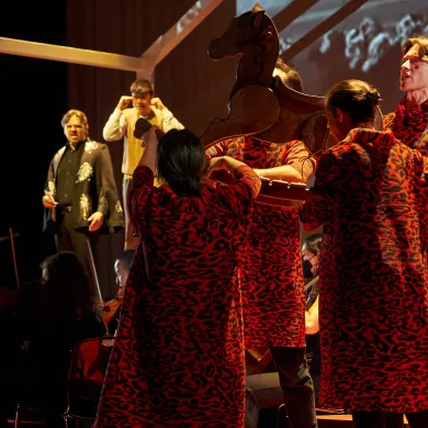 Performers in red patterned costumes holding a wooden horse prop on stage.