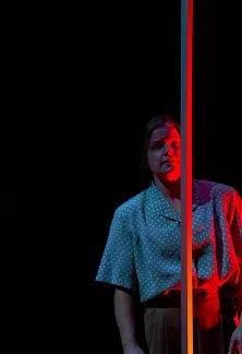 Actor standing beside a vertical light strip on a dark stage.