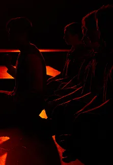 Silhouettes of performers sitting in red stage lighting.