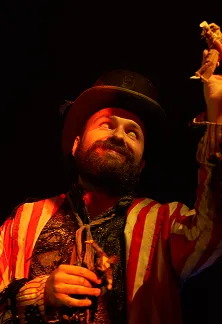 Performer in a top hat smiling and raising their hand under dramatic lighting.