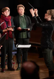 Choir standing and singing while a conductor leads them.