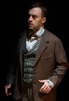 Actor in vintage clothing looking concerned on a dark stage.