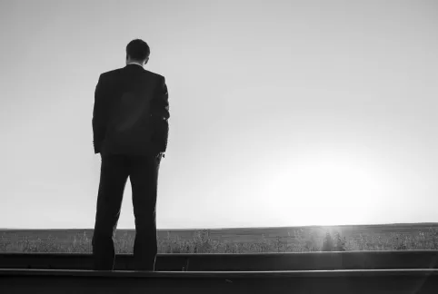 Man in a suit standing on railroad tracks, watching the sunrise.
