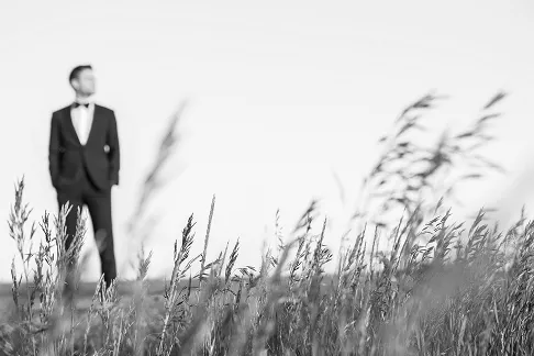 Blurry foreground grass with a man in a suit standing in the background.