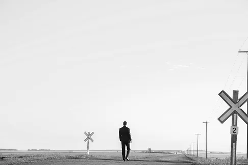 Man in a suit walking alone down an empty rural road.