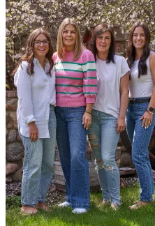 Four women smiling and standing together in a garden.