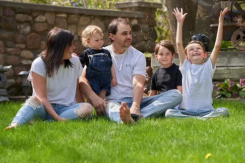 Family sitting together on the grass, with a child happily throwing their arms up.
