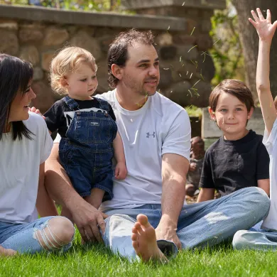 Family sitting together on the grass, with a child happily throwing their arms up.