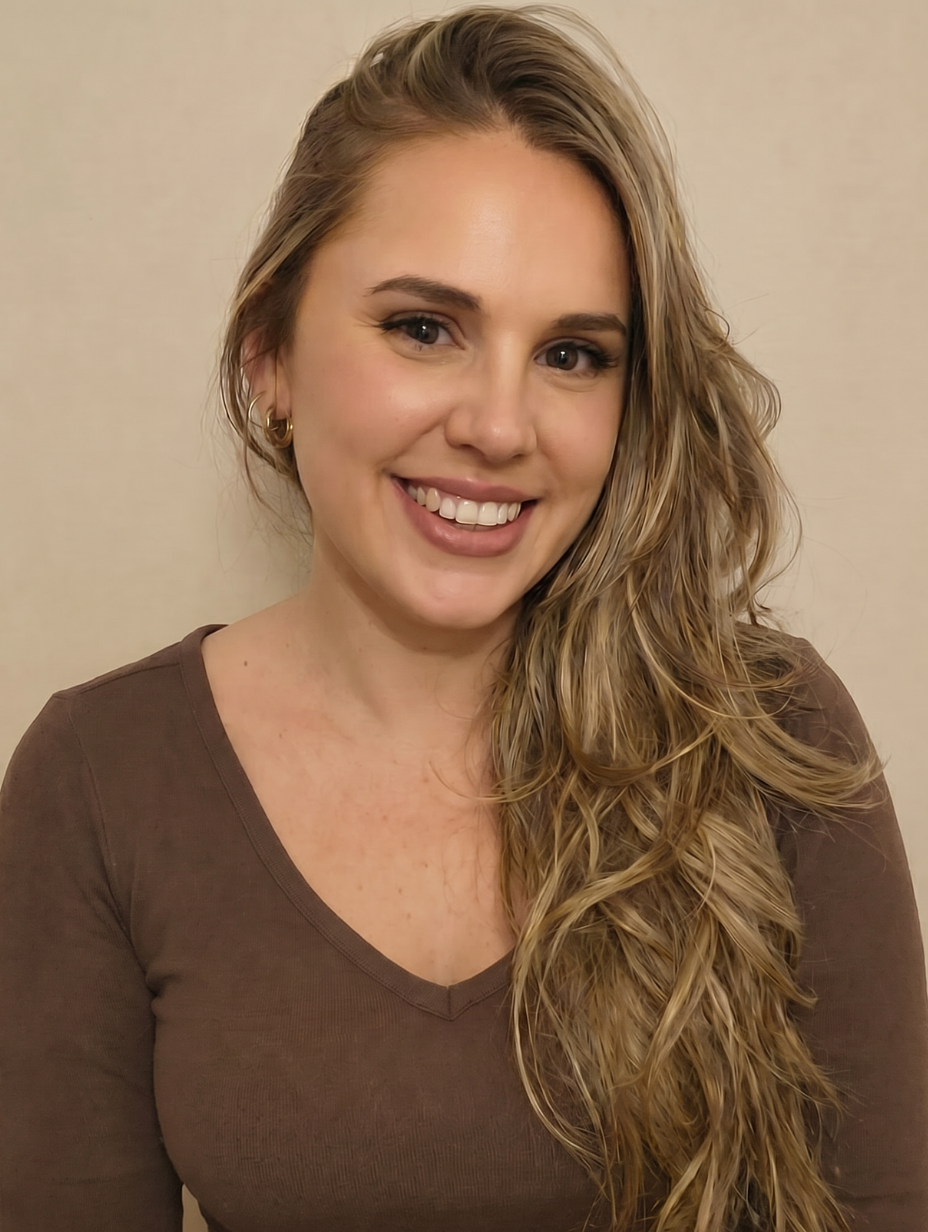 Femme blonde souriante portant un blazer beige avec de grands anneaux dorés, posant les mains croisées.