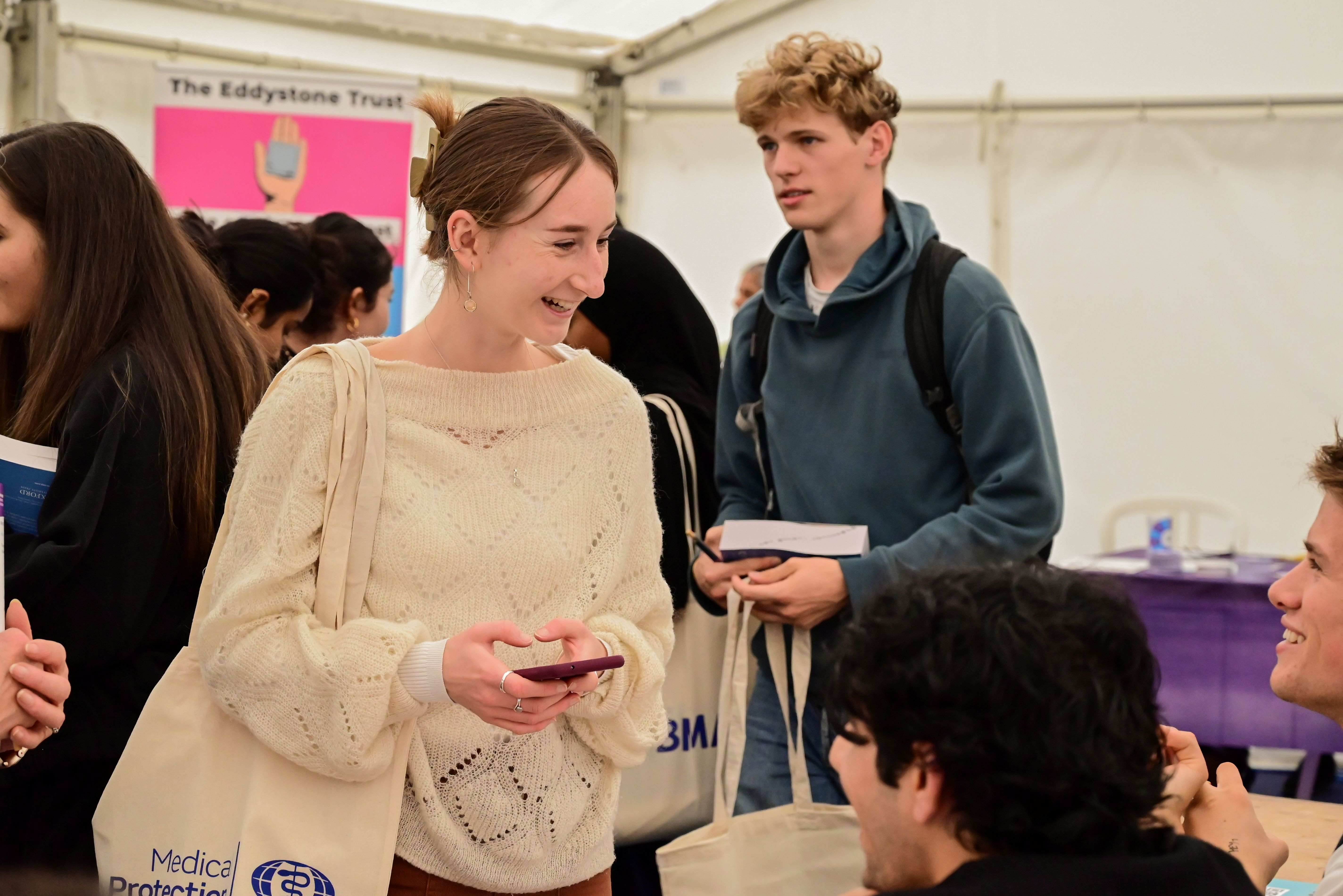Student holding a phone otalking to a student off camera 