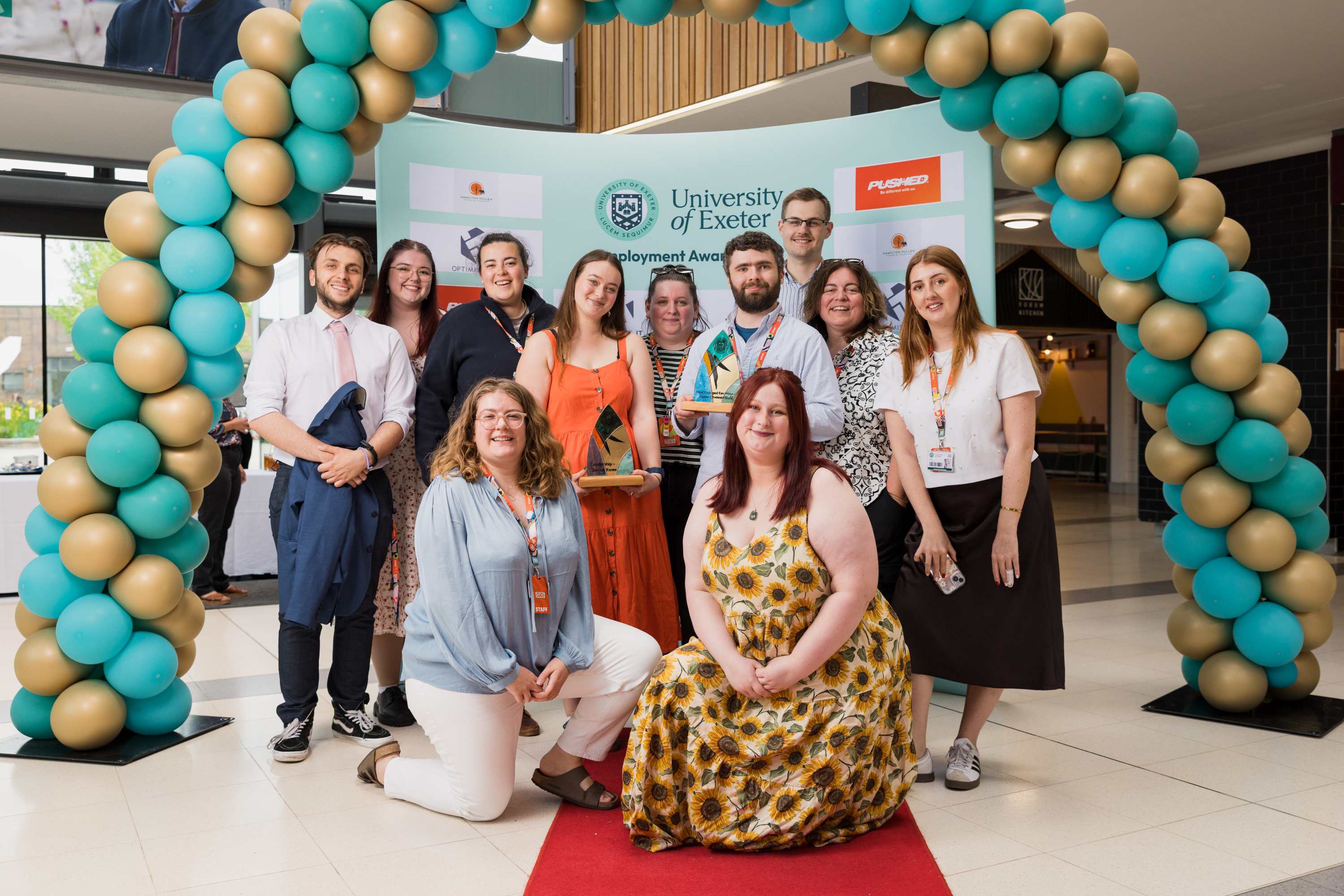 Staff in front of a balloon arch holding an award
