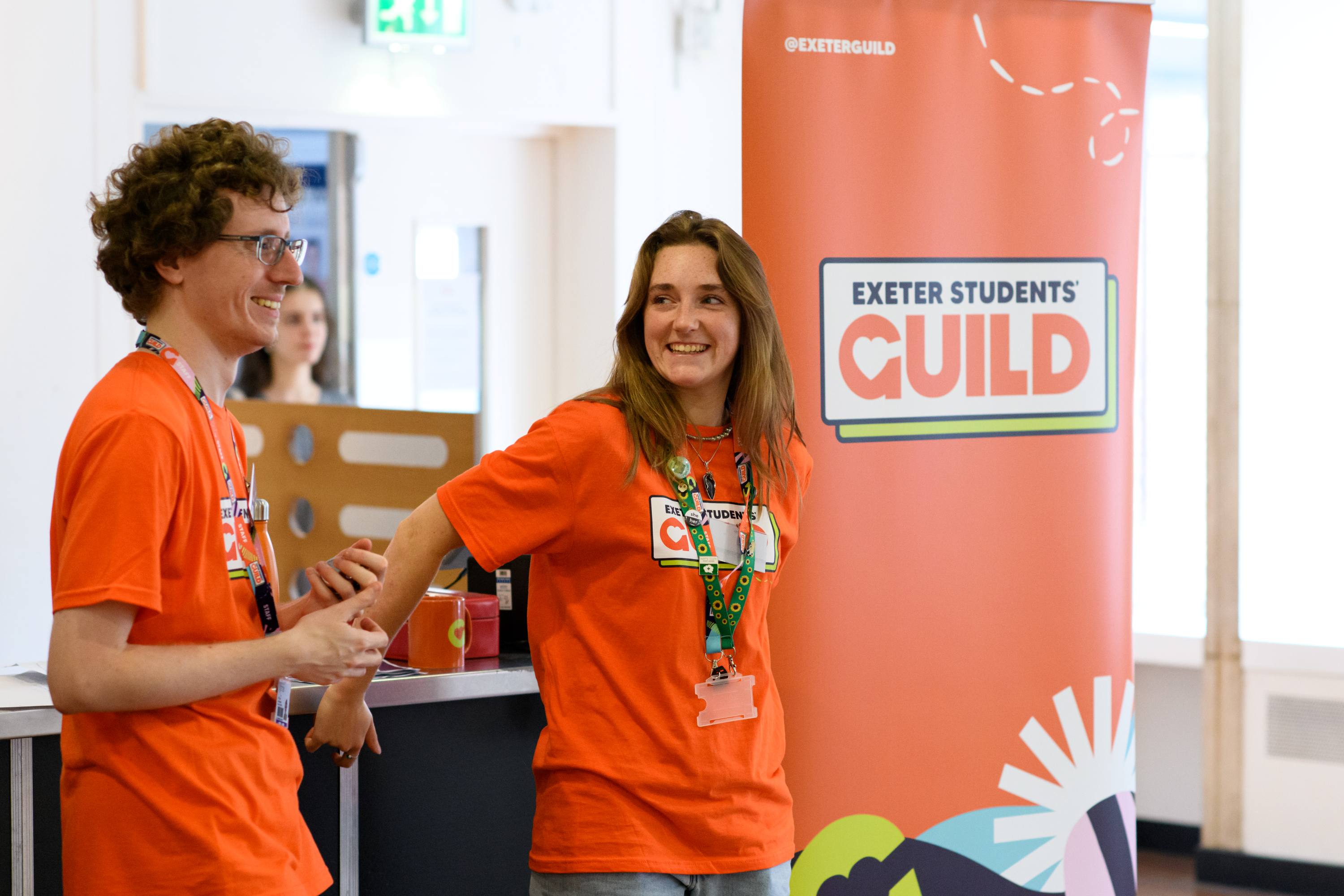 Two people in orange t-shirts talking to students
