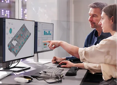 Two colleagues discussing data displayed on dual computer monitors in an office setting.