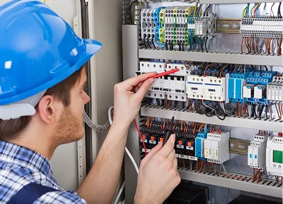Electrician in a blue hard hat working with wires inside an electrical control panel.